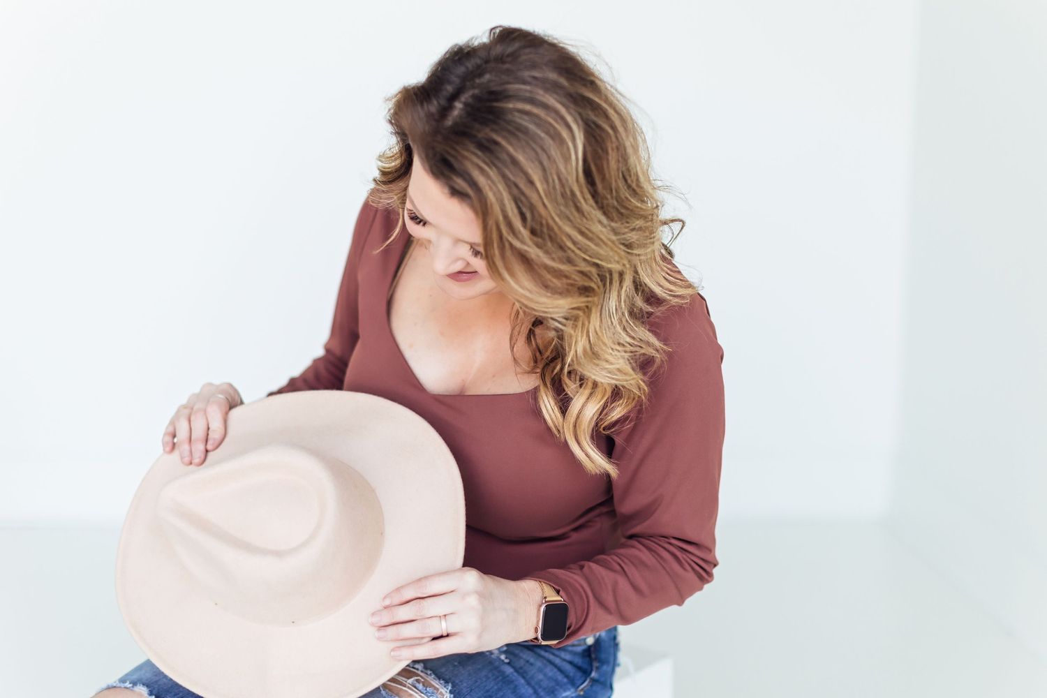 Woman in burgundy top looking down at beige hat while seated.