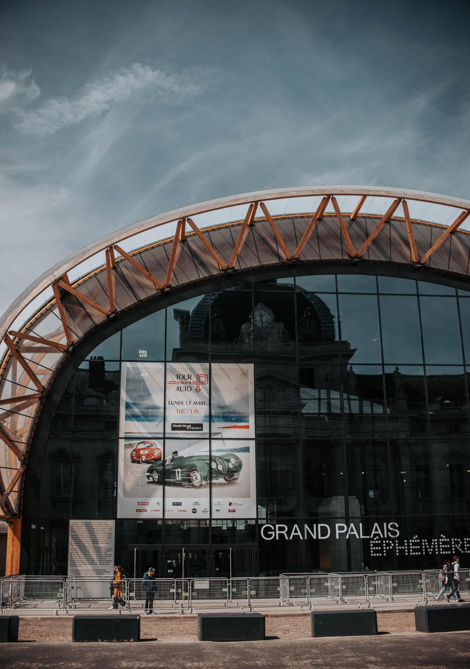 Modern glass and metal architecture of Grand Palais building under cloudy sky.