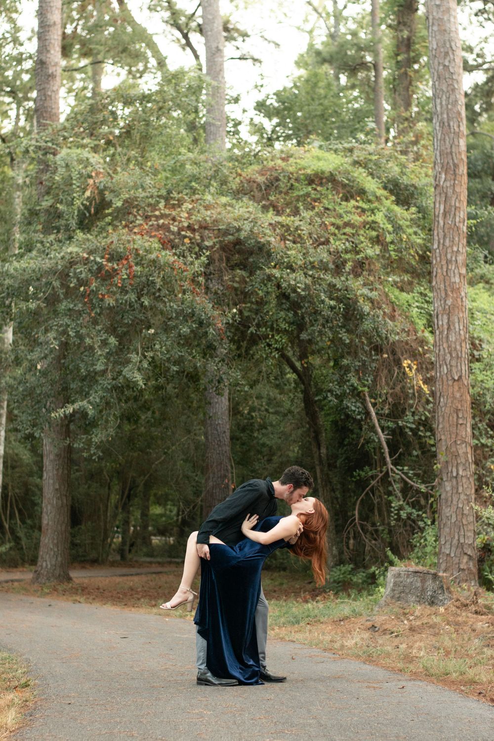 A romantic dip pose on a tree-lined pathway in the woods.