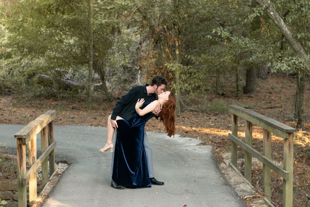 A couple shares a romantic dance on a wooden bridge surrounded by trees.