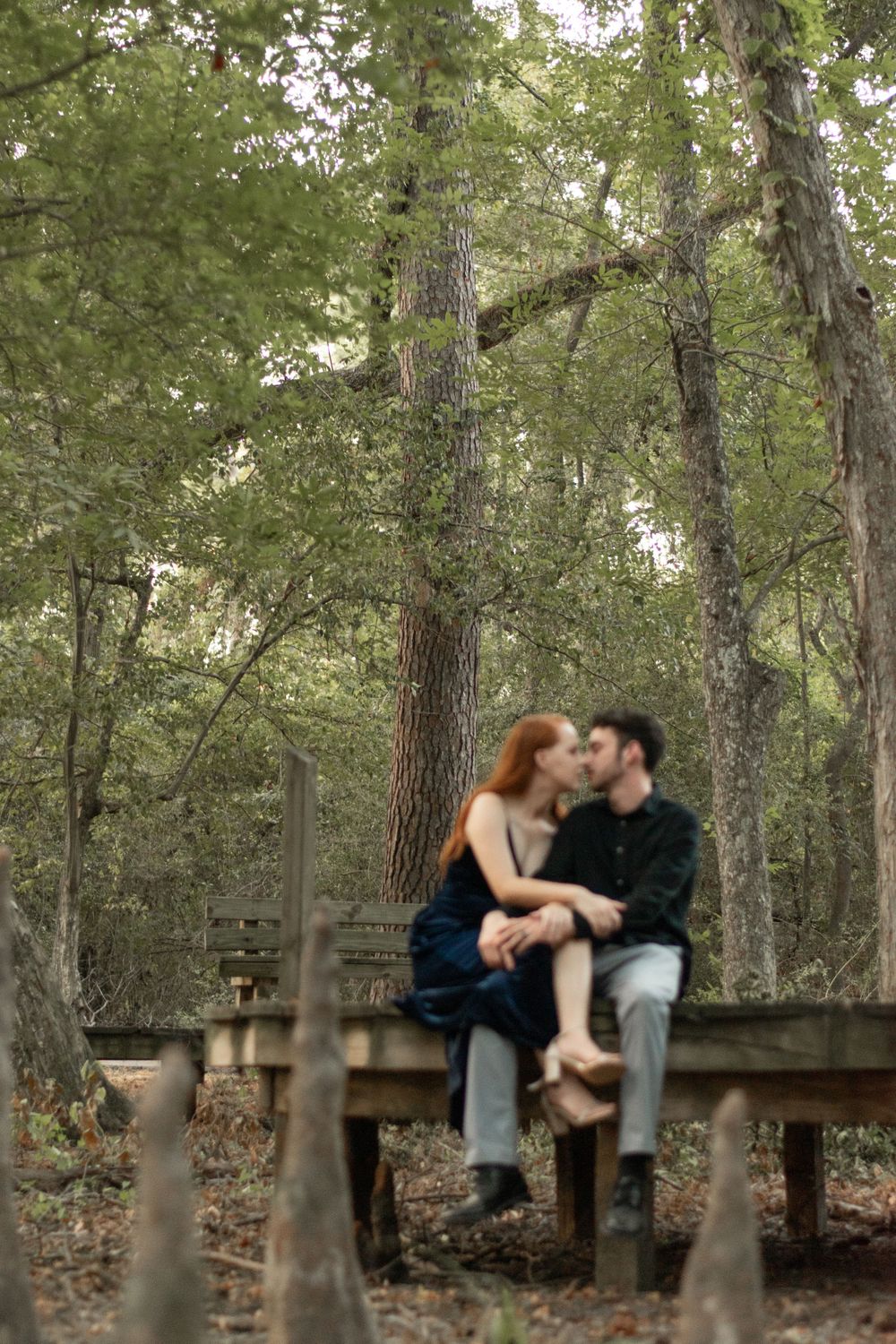A romantic moment shared on a wooden boardwalk in a wooded forest setting.
