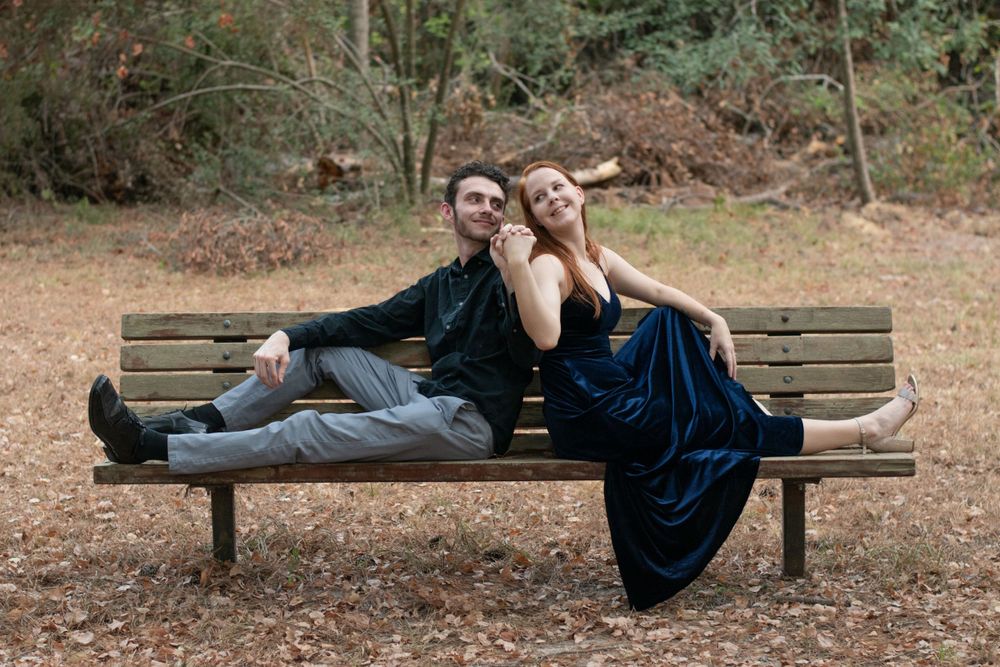 A romantic couple lounges on a wooden park bench surrounded by autumn foliage.