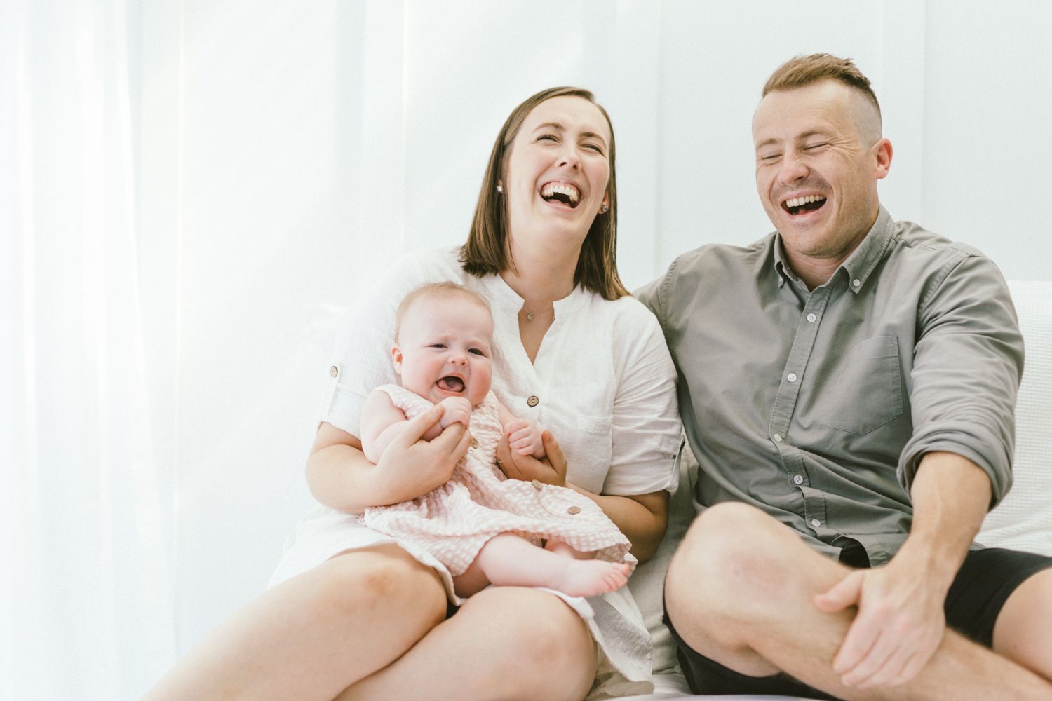 Family shares joyful moments with baby on white bed during casual indoor photoshoot.