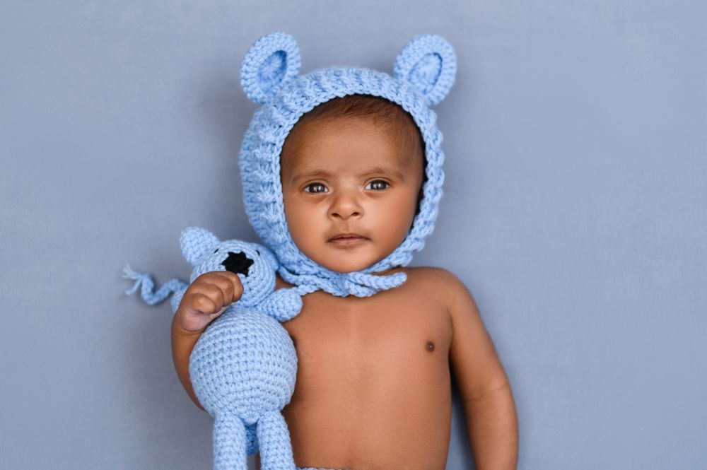 Infant wearing a light blue crocheted bonnet lying peacefully against a pale blue backdrop.