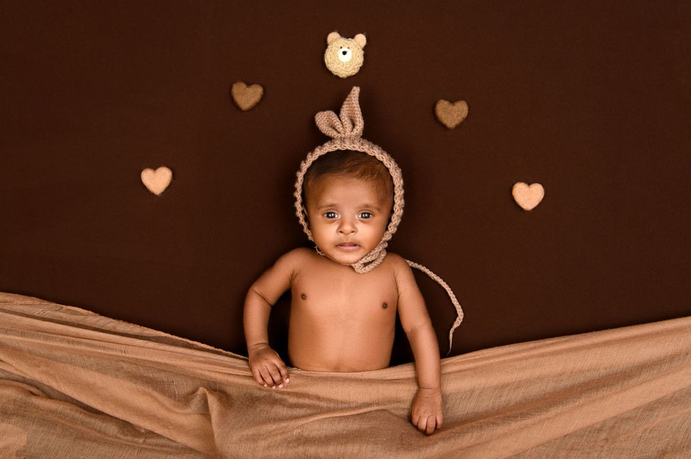 Artistic newborn photography with heart decorations on dark brown background.