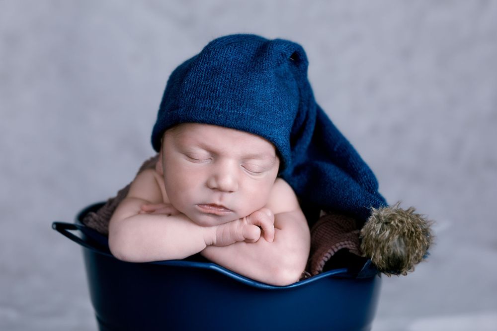 Sleeping newborn wrapped in navy blue blanket against neutral background.
