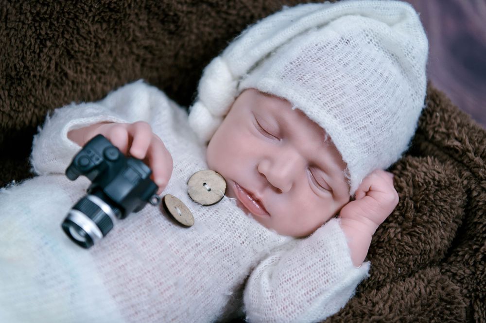 Adorable newborn photography session featuring a tiny baby wearing a blue knitted bonnet on a soft white blanket.