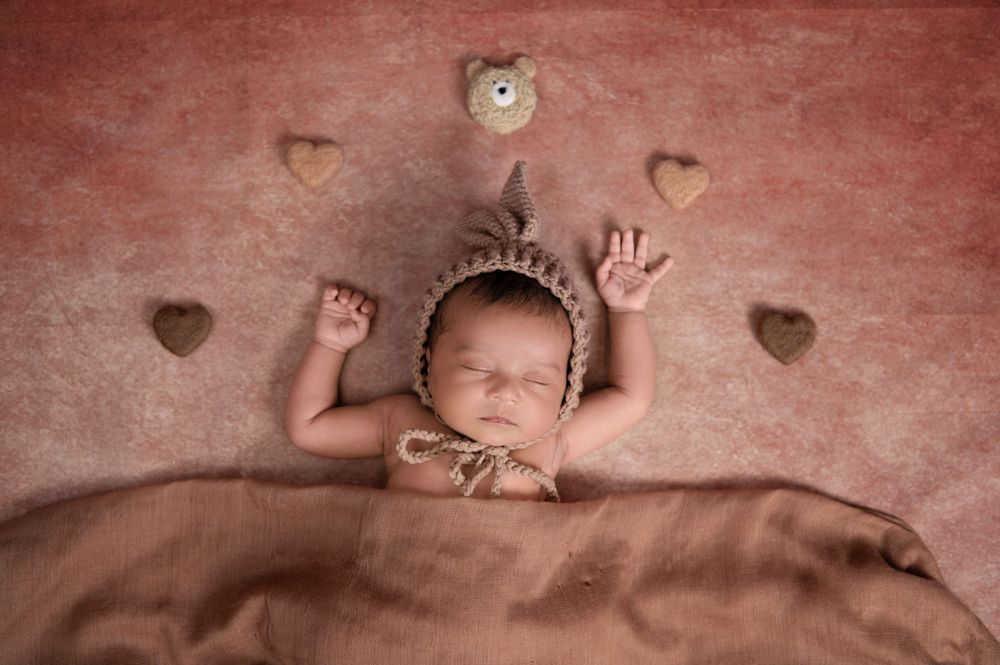 Sweet newborn portrait with heart decorations against a textured red background.