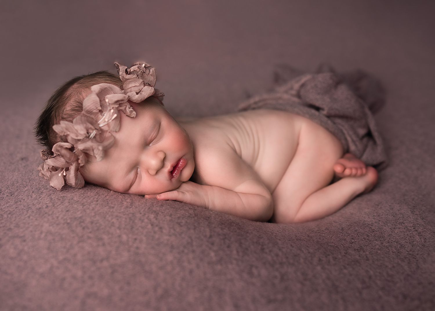 Peaceful sleeping newborn baby girl on mauve blanket with floral headband.