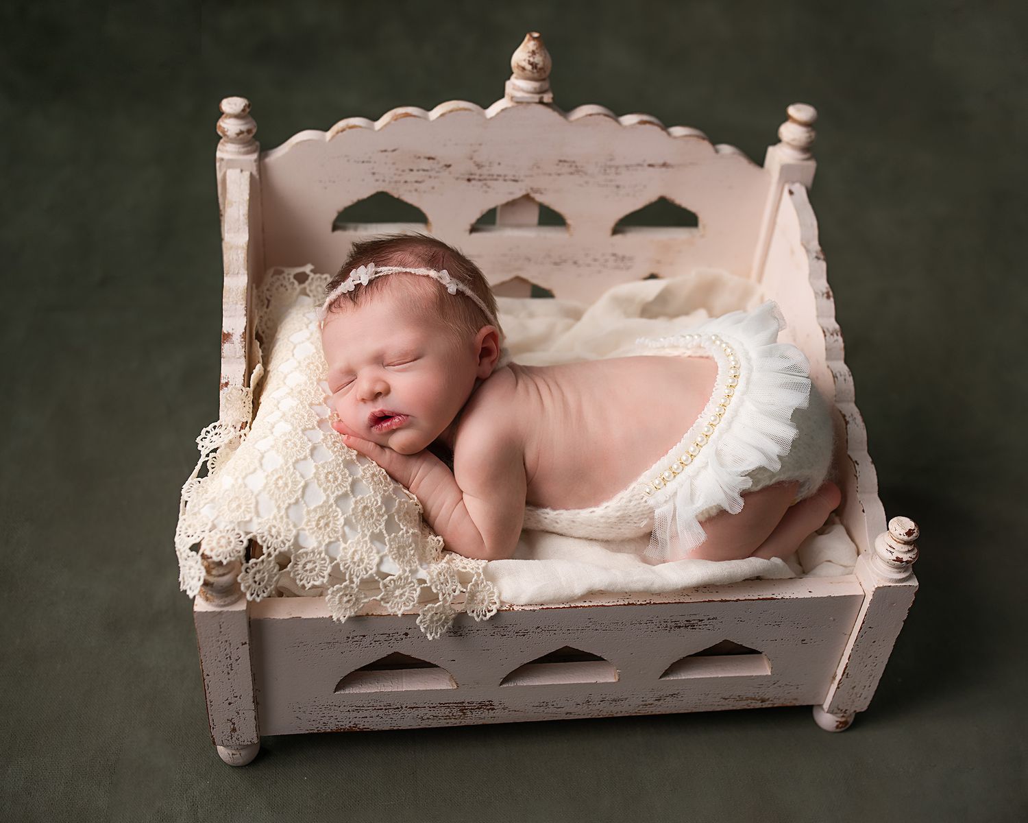 Sleeping newborn baby girl on vintage white miniature bed prop.