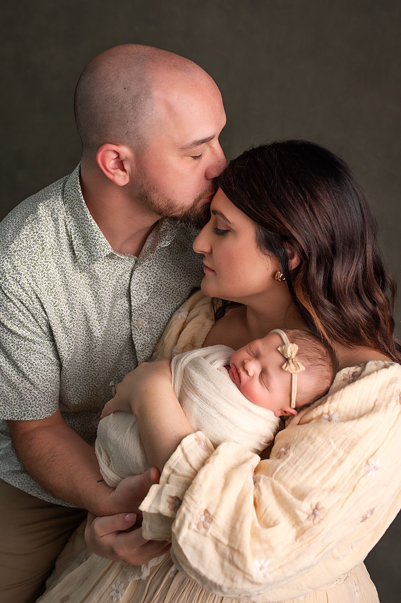 Parents lovingly holding sleeping newborn baby girl in studio portrait.