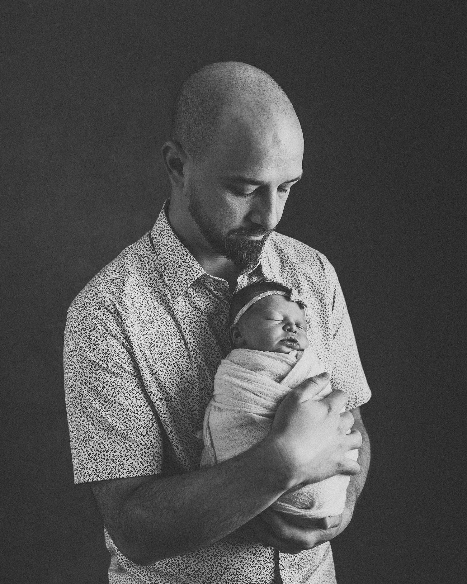 Father holding newborn baby in black and white studio portrait.
