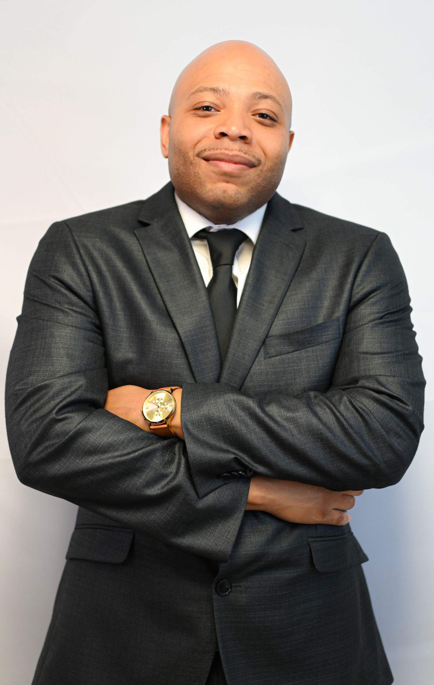 Professional in dark suit and tie poses confidently against white background.
