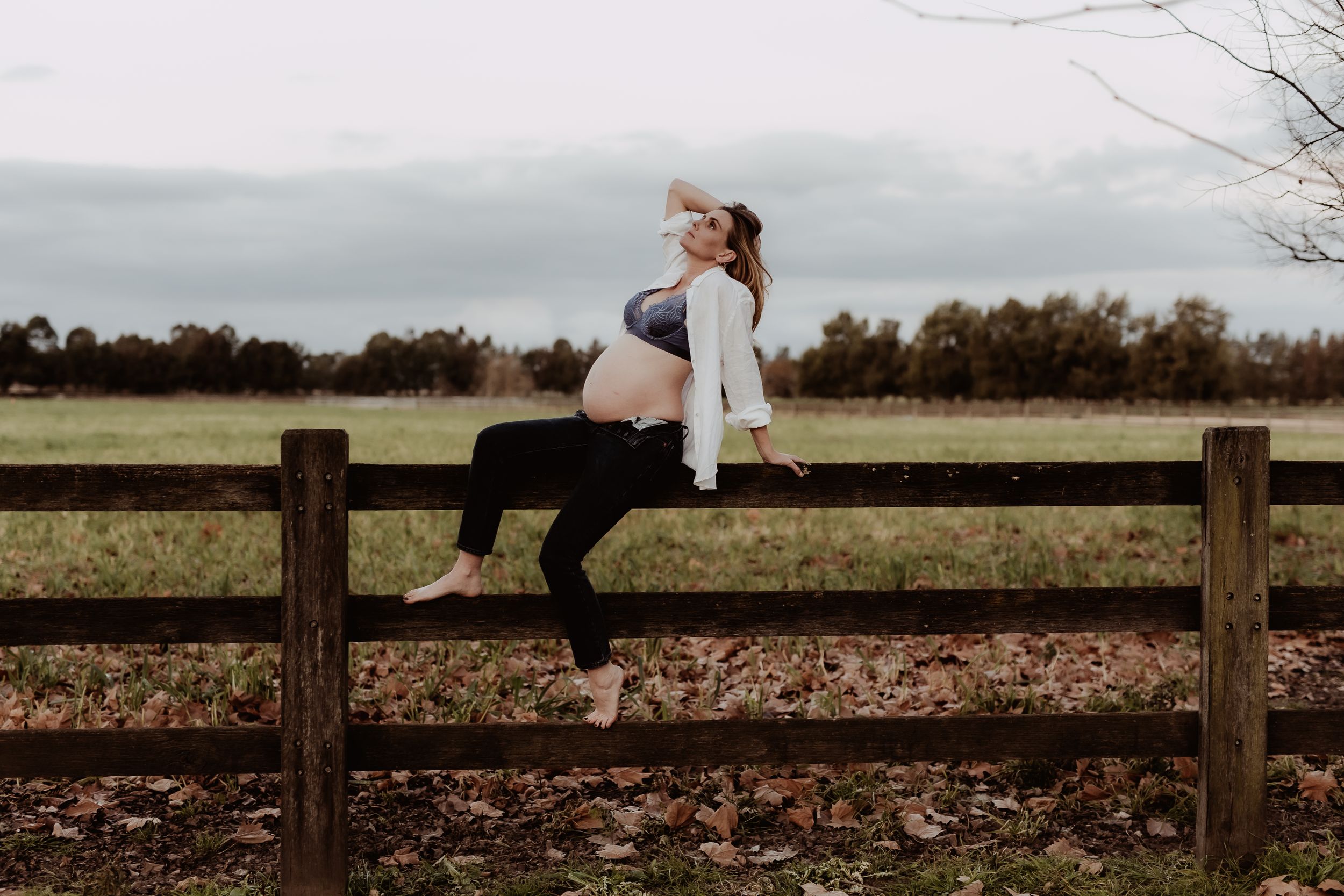 Two people relaxing on a wooden fence surrounded by fallen autumn leaves.
