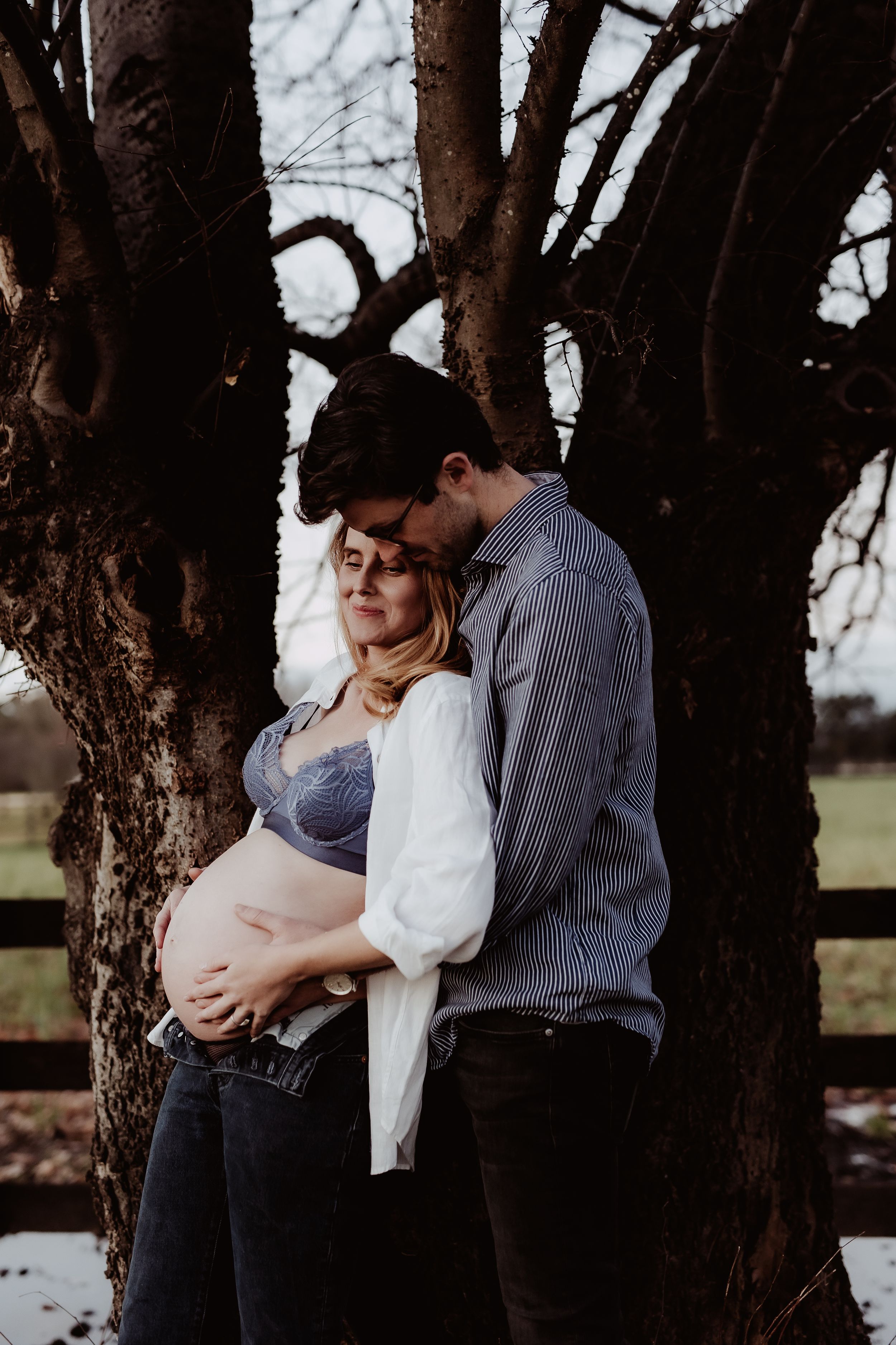 Intimate couple embracing against a tree trunk in a romantic outdoor setting.
