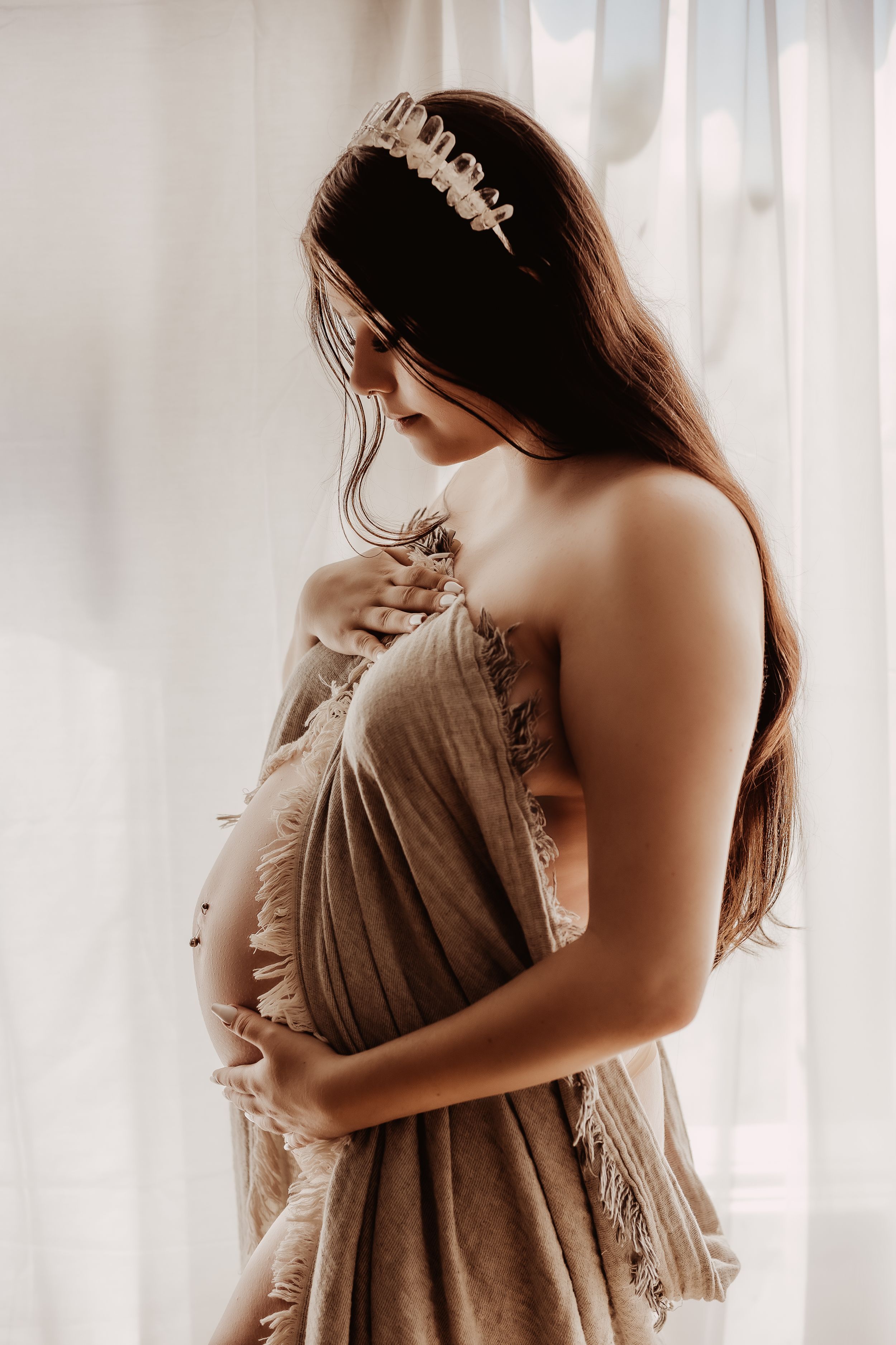 Artistic maternity portrait with flowing dress against white curtains in natural light.