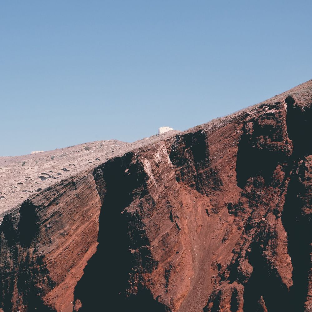 A reddish-brown rocky mountain slope with a small structure visible at the summit.