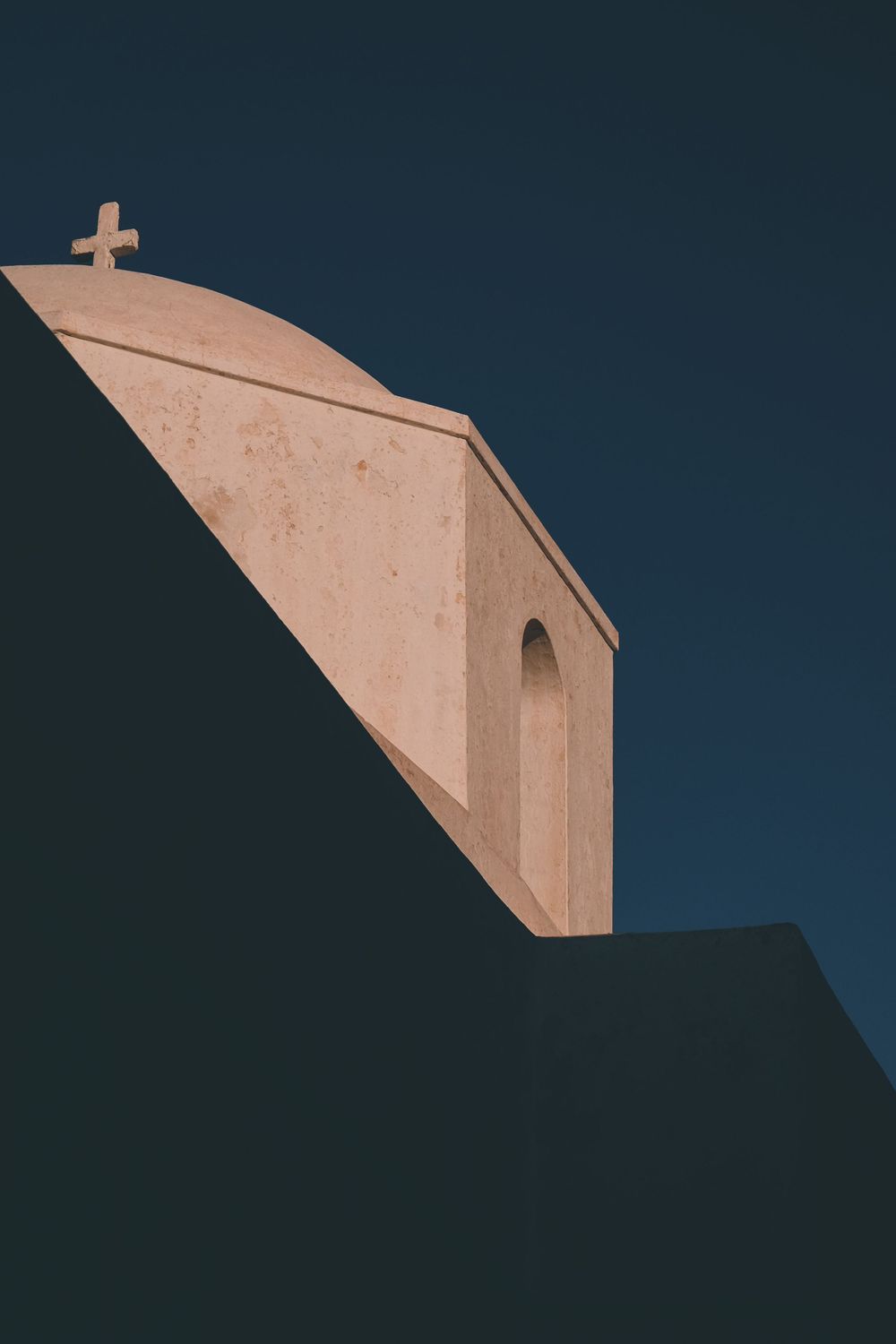 Minimalist architectural detail of a white church steeple with cross against dark sky.
