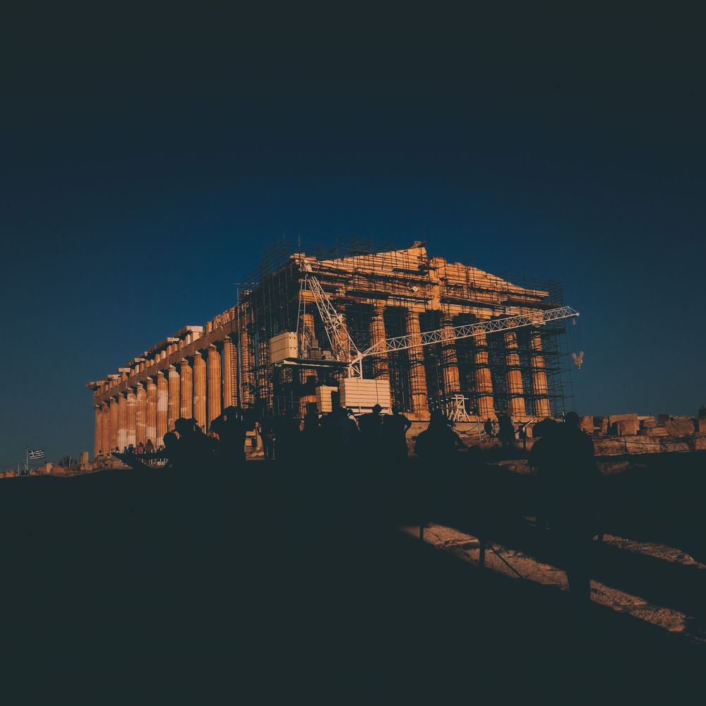 Ancient Greek temple ruins illuminated at dusk against a deep blue sky.