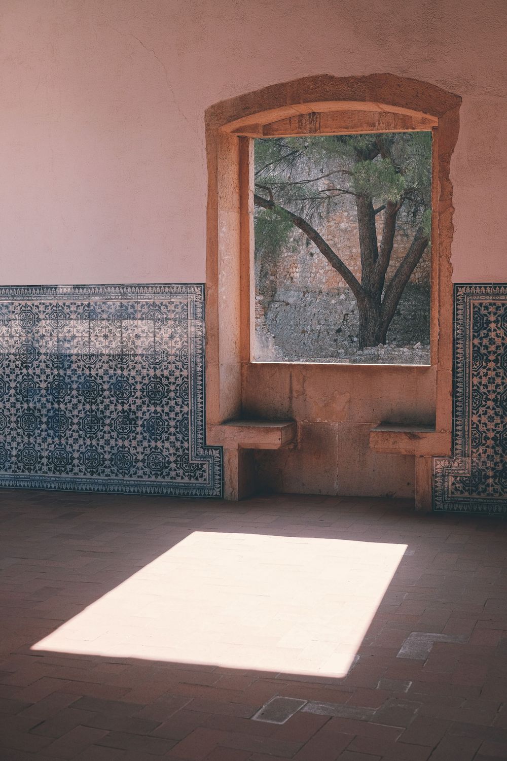 Sunlight streams through a window onto a tiled floor beside decorative wall patterns in a historic building interior.