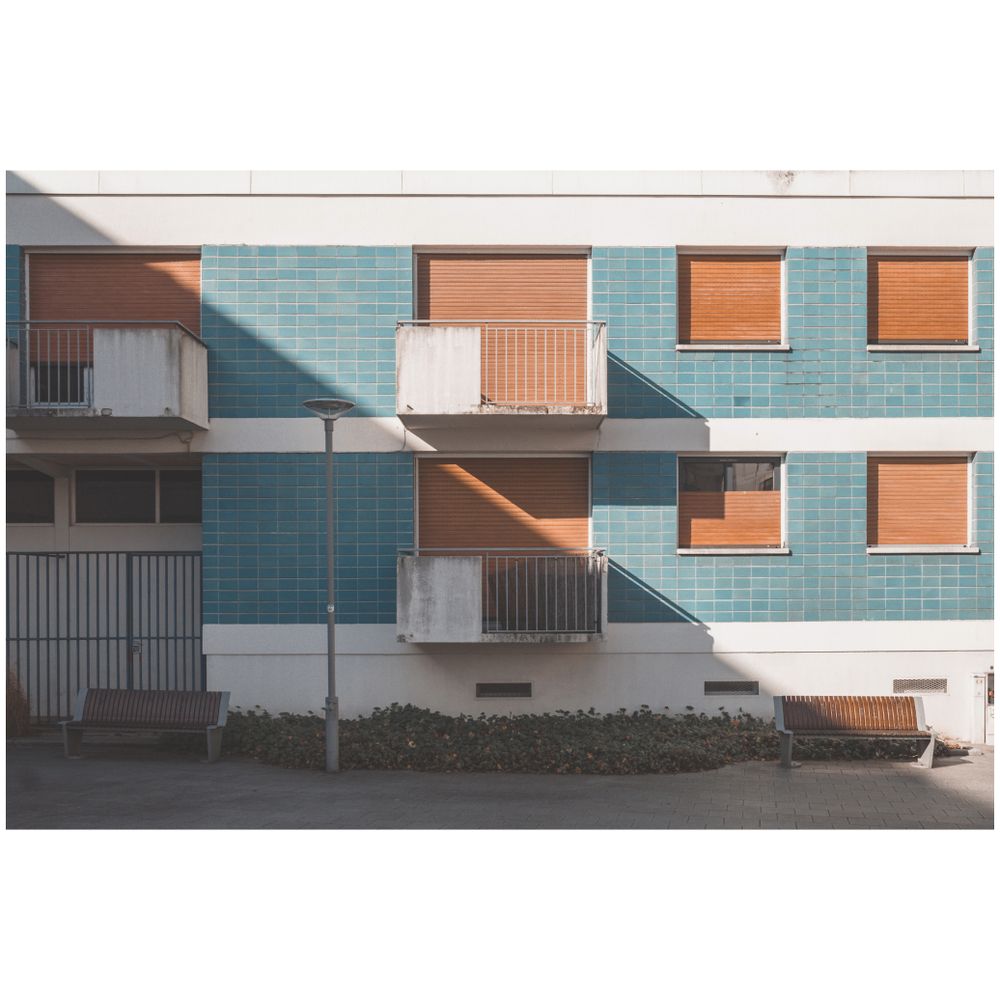 Modern apartment building exterior with turquoise tiles and white balconies casting geometric shadows.