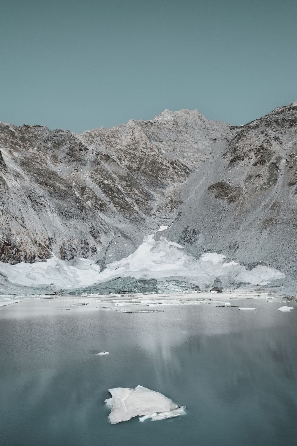 Snow-capped mountain peaks reflect in a glacial lake with floating ice chunks.