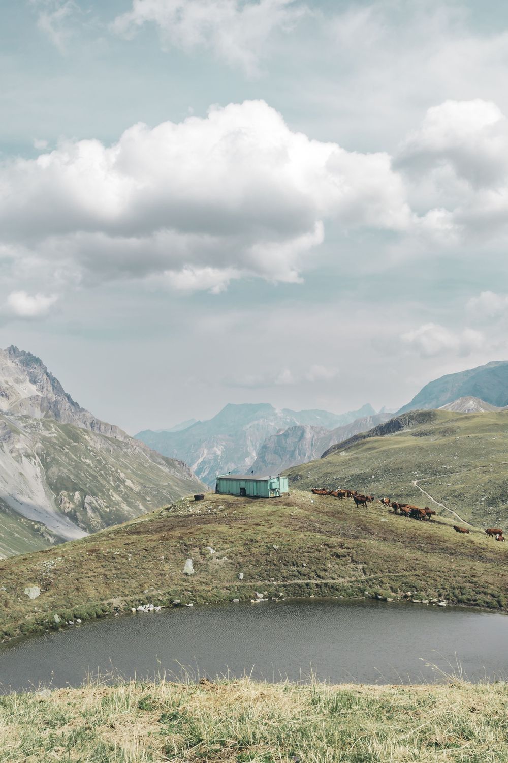 Small mountain hut overlooking an alpine lake with dramatic mountain peaks in the background.