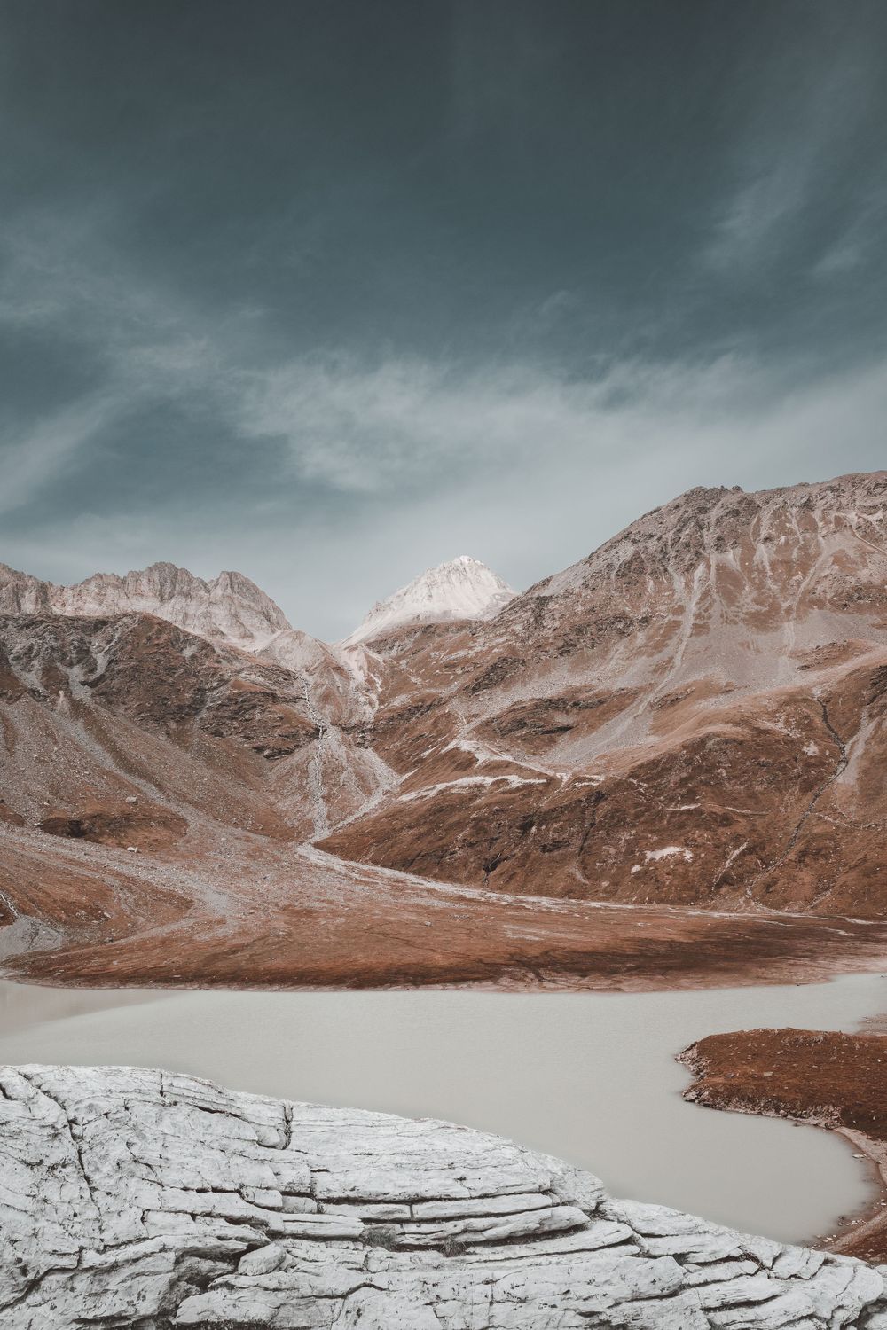 Dramatic mountain landscape with brown rocky peaks surrounding a glacial lake.