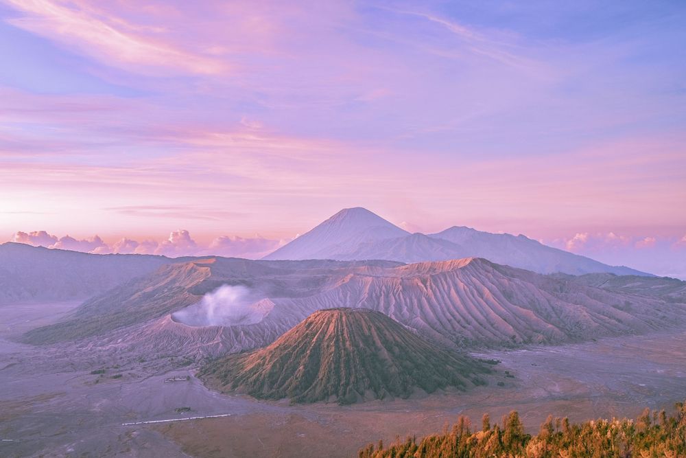 Majestic volcanic peaks at sunrise with misty valleys and purple-pink sky in Mount Bromo, Indonesia.