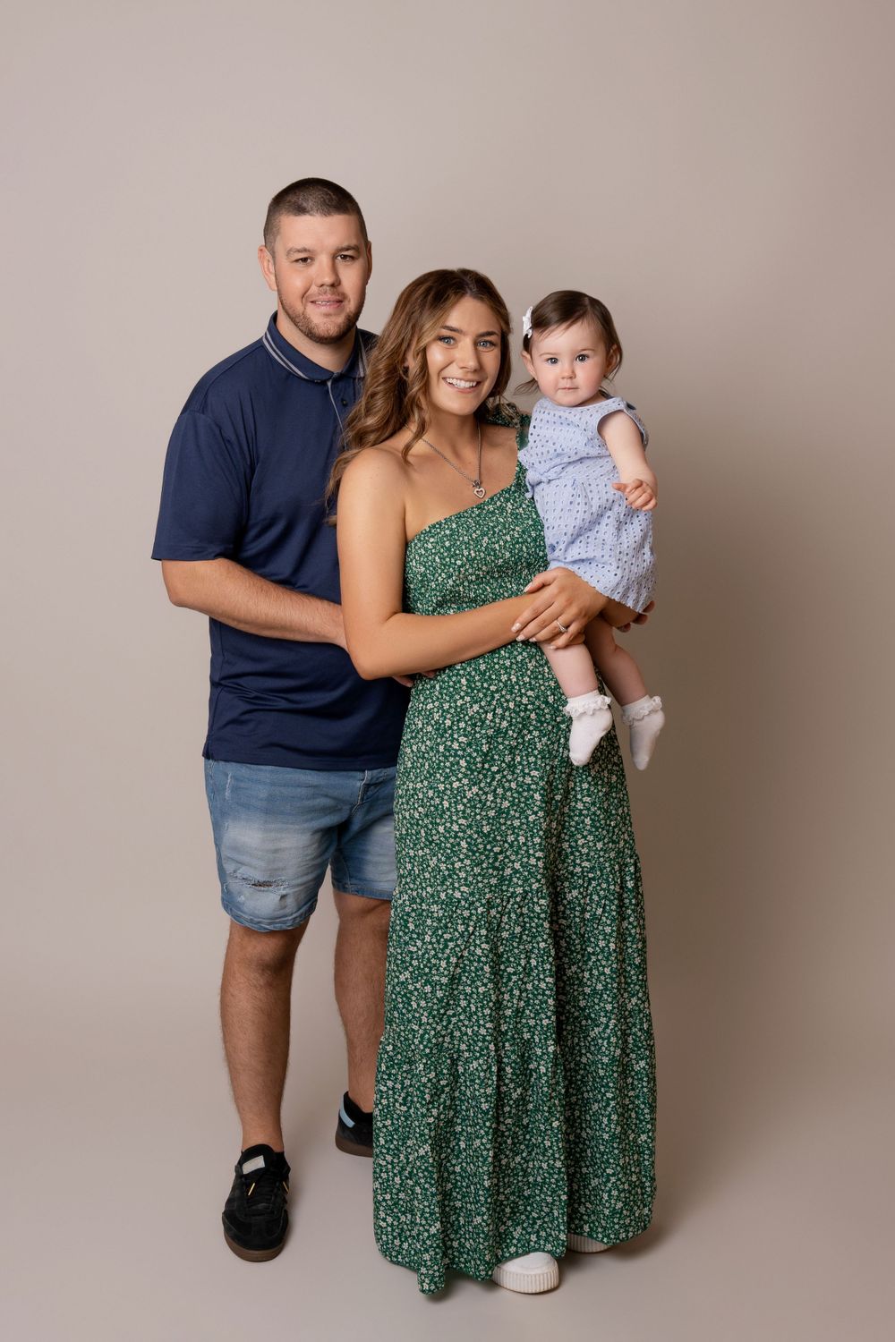 Family portrait with woman in green floral dress and baby in blue outfit.