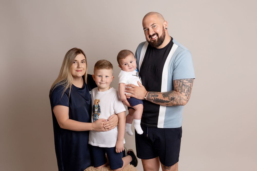 Casual family portrait with parents and children in navy and white against gray backdrop.