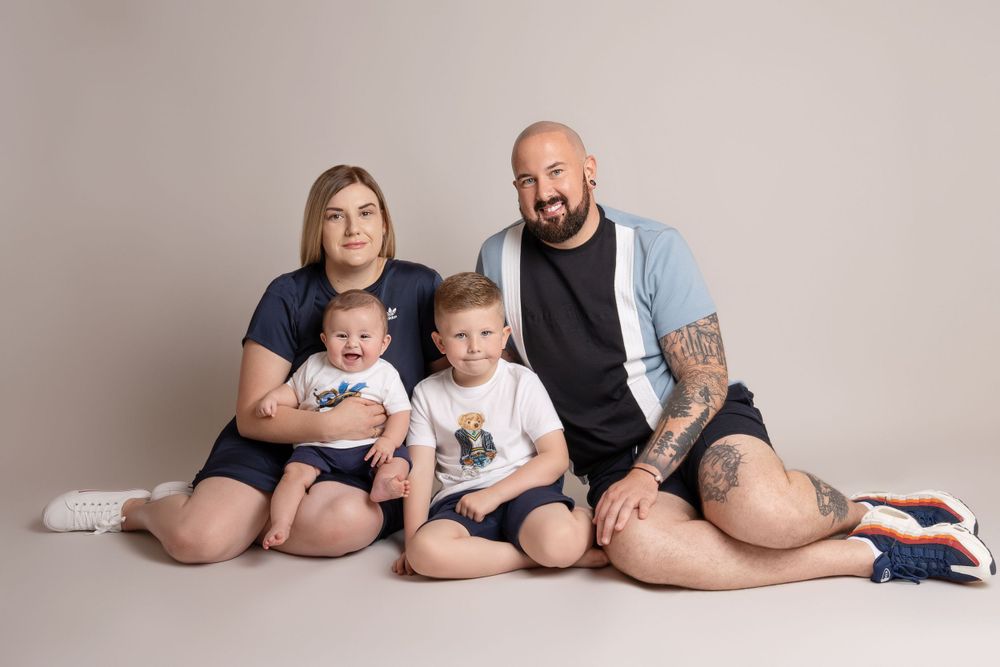 Casual family portrait sitting together on floor wearing coordinated navy and white outfits.