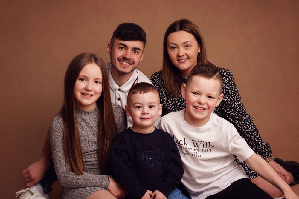Studio family portrait with brown backdrop featuring coordinated casual outfits.