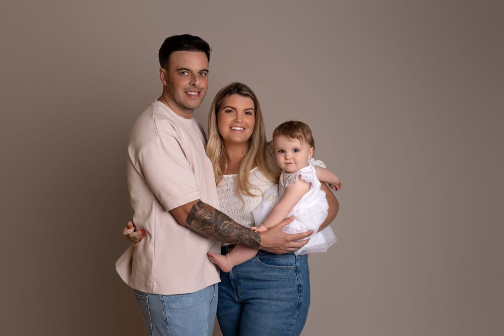 Studio family portrait with neutral background and coordinated casual outfits.