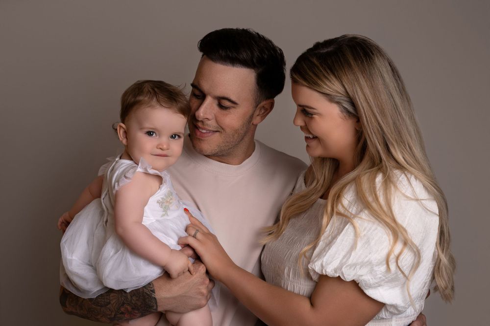 A heartwarming family portrait with a baby in white against a neutral background.