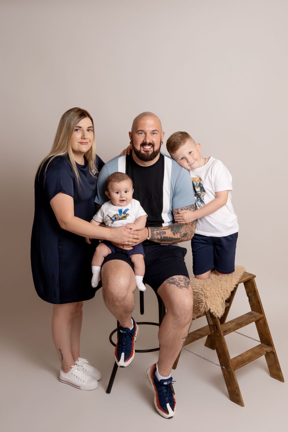 Family portrait featuring matching blue and white outfits with a rustic wooden step stool prop on neutral background.
