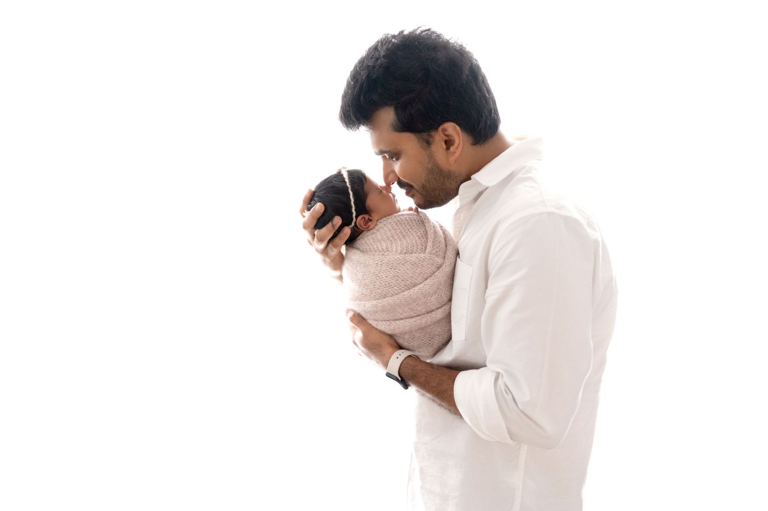 Parent in white shirt holding and gazing at swaddled newborn against white background.