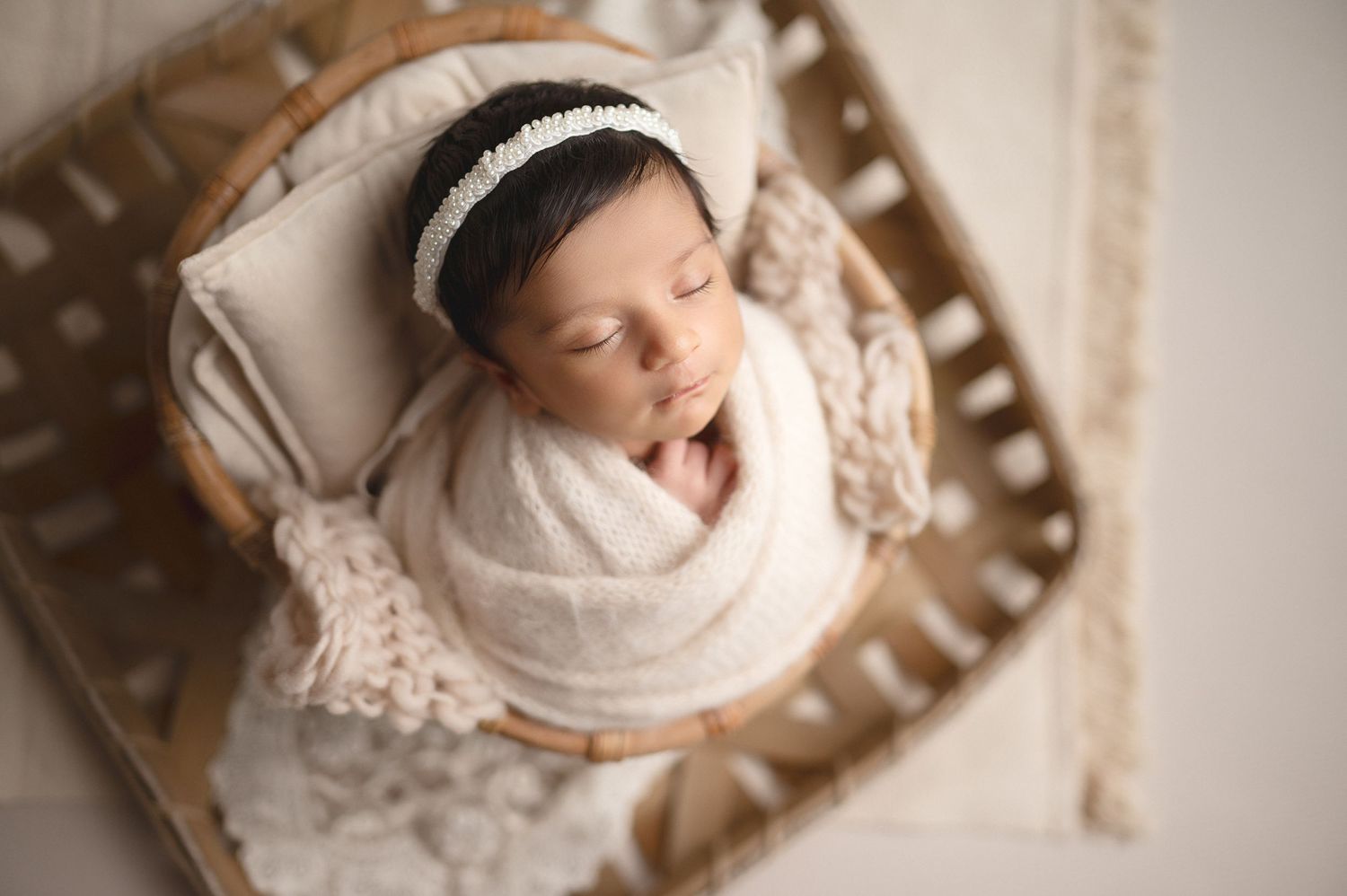 Wrapped newborn sleeps in wooden bowl with lace details during professional photo shoot.