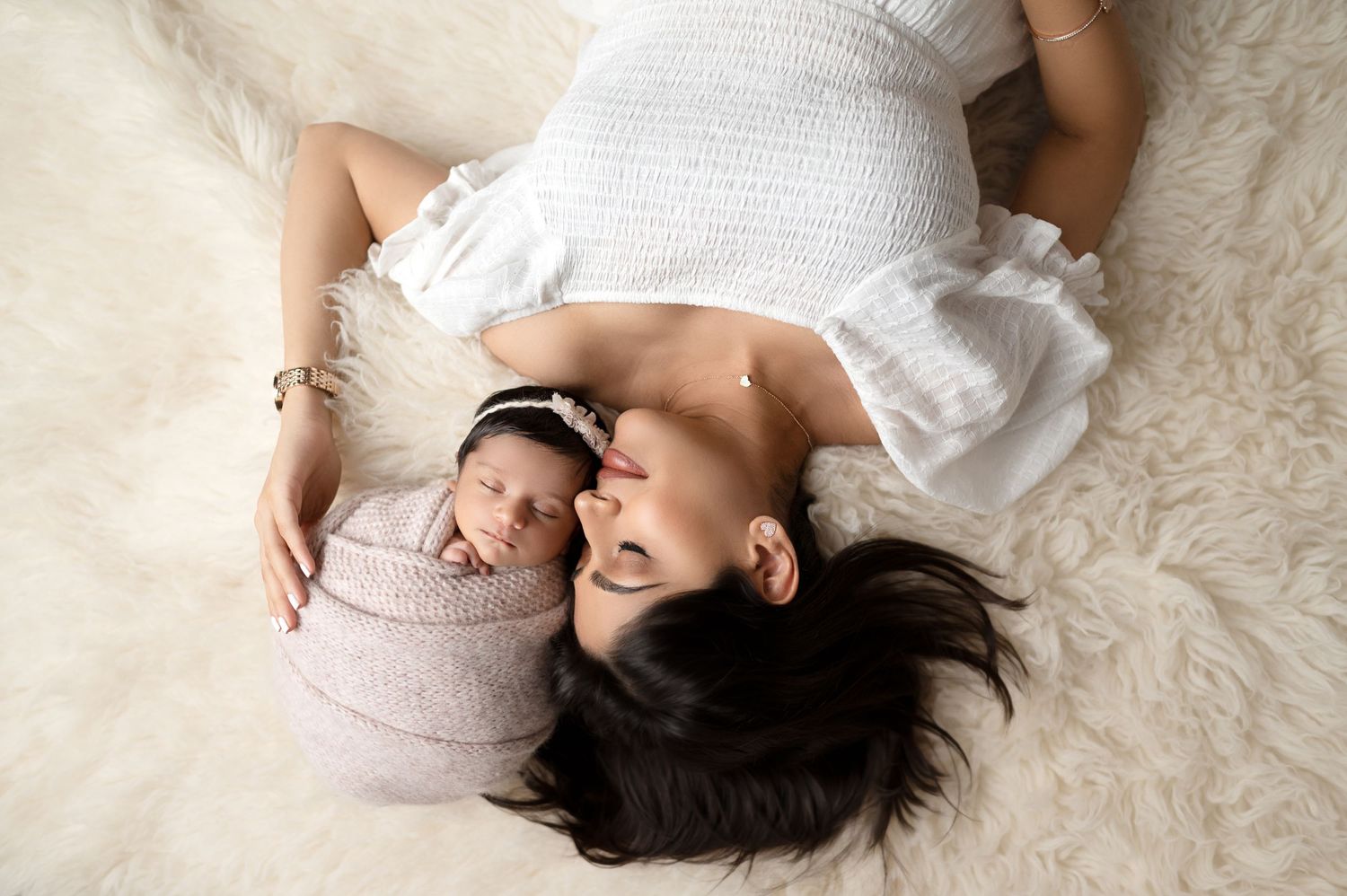Overhead view of parent and newborn lying together on white textured blanket.