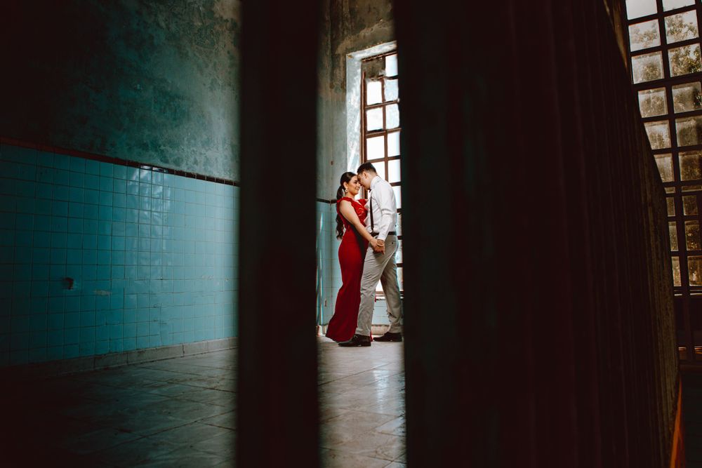 A couple shares an intimate moment in dramatic lighting through a window frame.