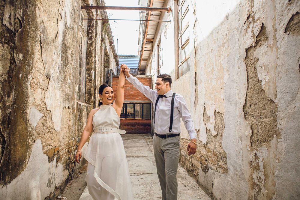 A couple walks hand in hand through a rustic stone alleyway.