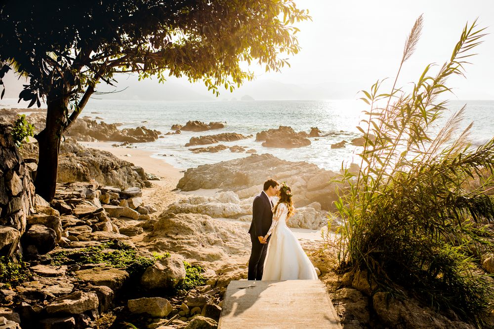 Coastal wedding scene at sunset with rocks and ocean in background.