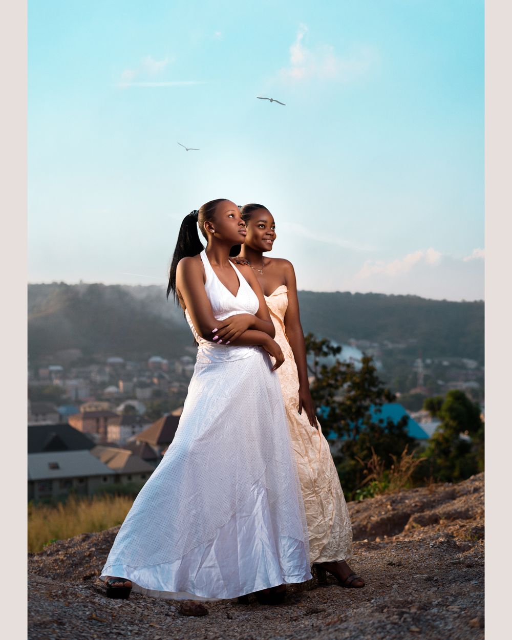 Two people in elegant white dresses posing against scenic mountain backdrop.