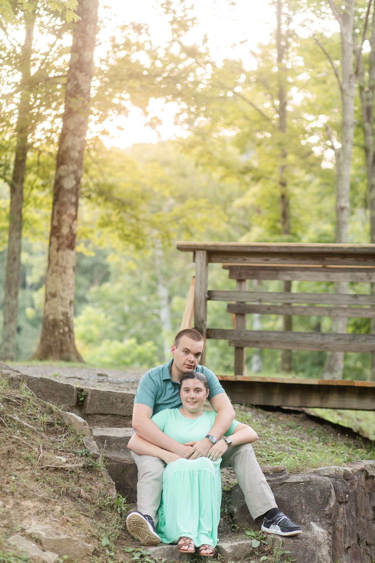 Two people sit together on stone steps in a wooded park setting during golden hour.