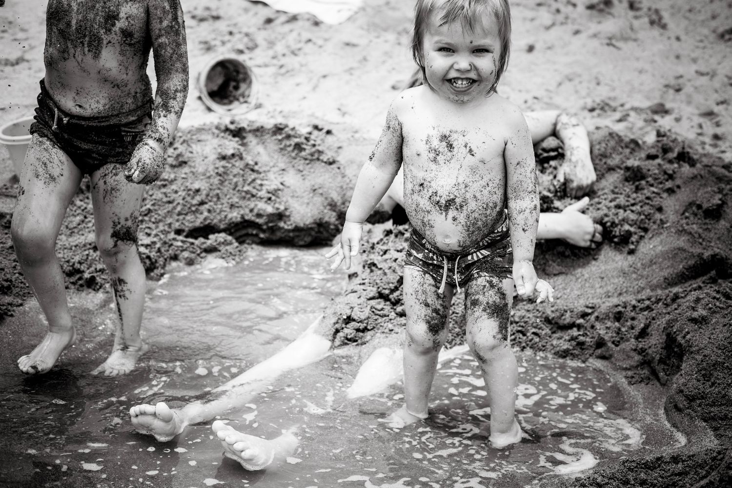 Toddler full of muddy sand covers his buddy smiling to the camera at Fuengirola beach.