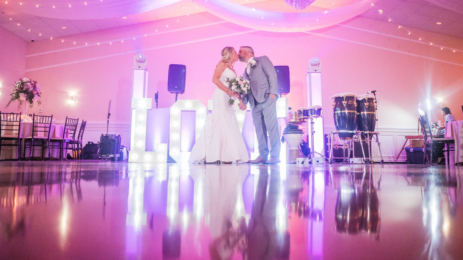 Romantic kiss as couple holds hands in the midst of the reception hall.