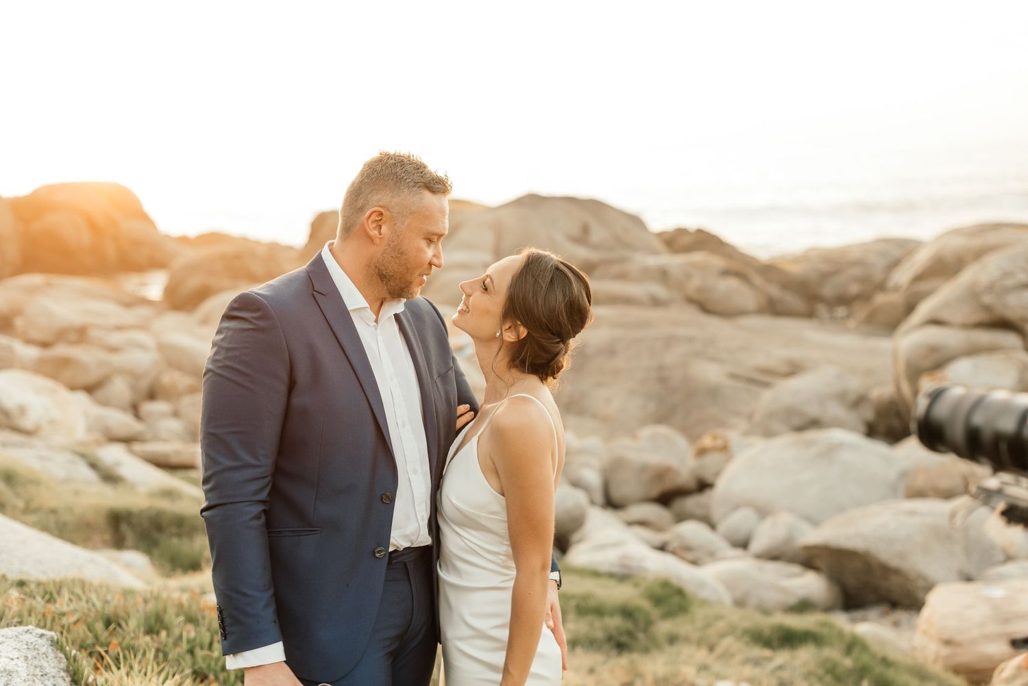 Bride and groom sharing a loving gaze at each other on a beach, illuminated by the breathtaking golden glow of the sun.