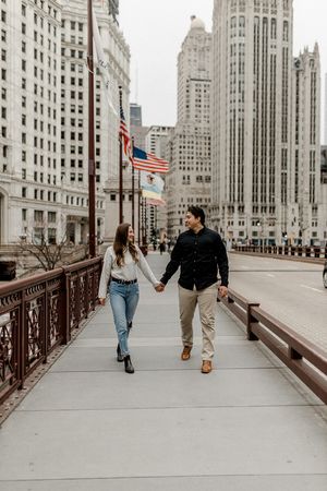 Couple walking hand in hand on Chicago bridge with American flags and iconic architecture.