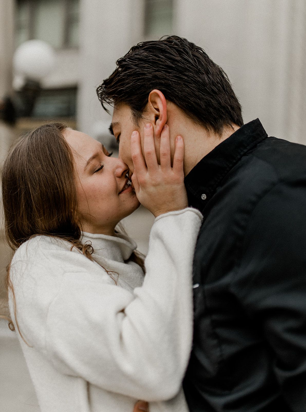Romantic couple sharing passionate kiss against neutral urban backdrop.