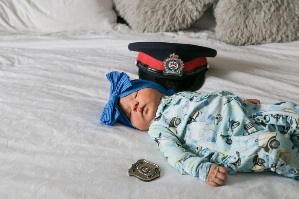 A baby laying on a bed with a police hat.